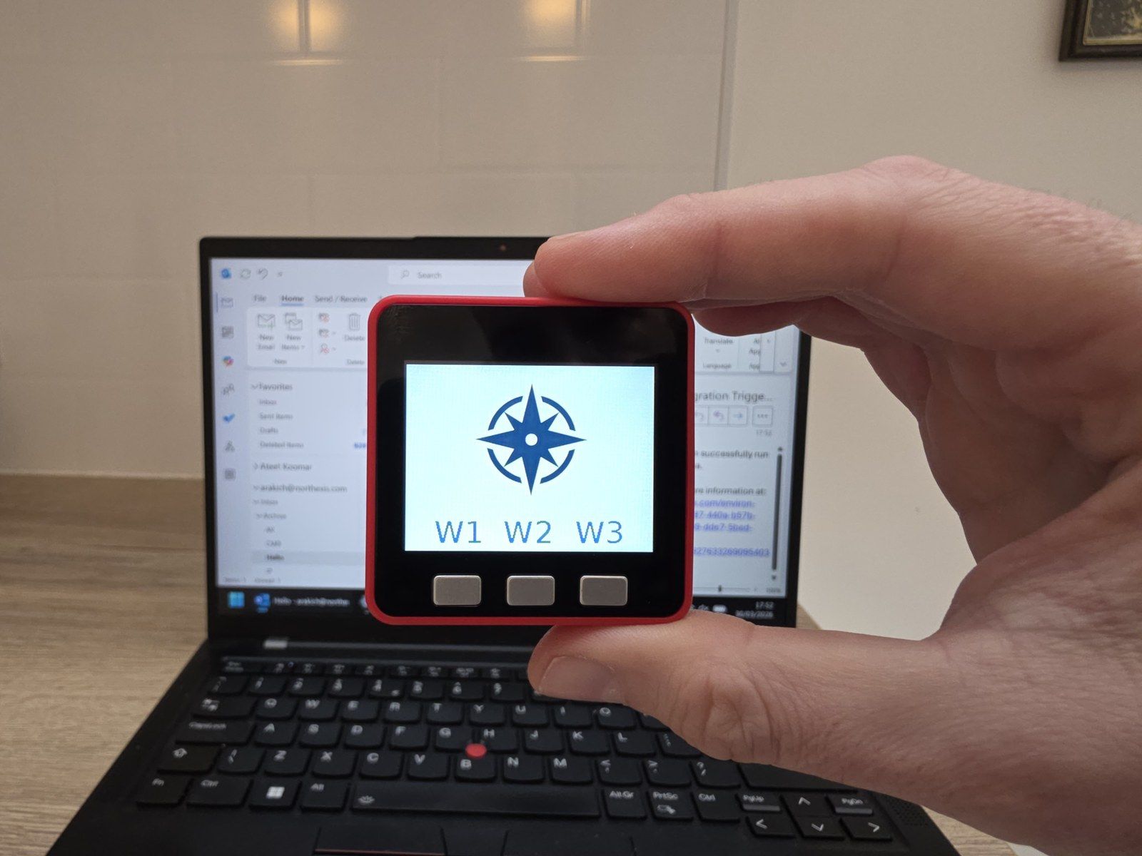 The Northexis Device, a small screen with a button, held up in front of a laptop
