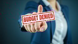 an accusing finger with a stamp saying budget denied-1
